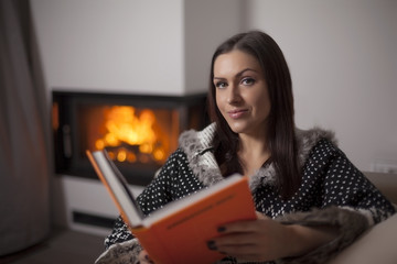 Portrait of beautiful woman reading book by fireplace