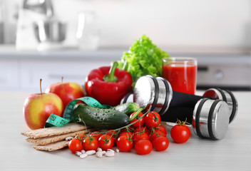 Set of fresh fruits and vegetables with dumbbells on wooden table closeup