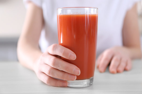Female hand holding glass of tomato juice on wooden table closeup