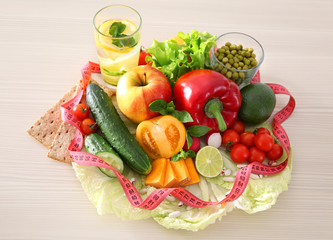 Fresh fruits and vegetables with measuring tape on wooden background
