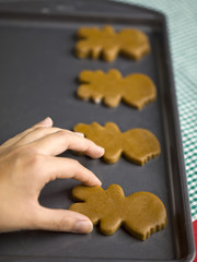 hand placing gingerbread men cookie on tray