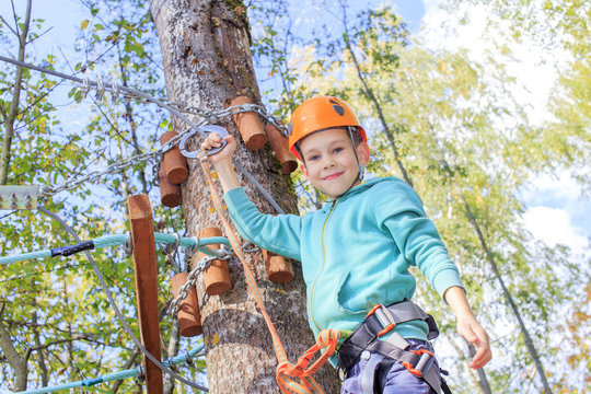 happy boy overcoming fear of heights. smiling child engaged climbing high wire park