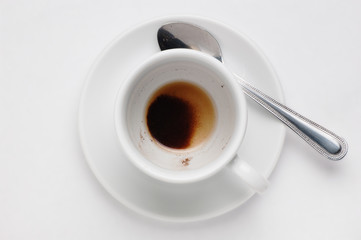 Drunk cup of coffee with coffee grounds on saucer against white background, top view with place for text