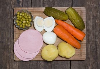 Ingredients for Olivier salad on the cutting board. Carrots, potatoes, cucumber, egg, sausage, green peas,