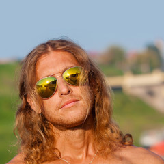 Handsome fitness model shirtless man walks along the beach in the city. Handsome man on the beach in sunglasses