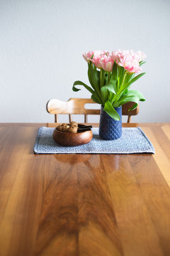 Tulips in blue vase and nuts in wooden bowl on wooden table. Selective focus.