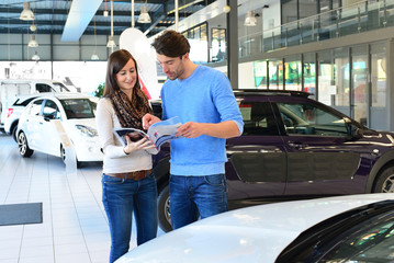 junges Paar im Autohaus - Verkaufsraum mit Neuwagen