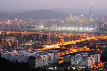 Panoramic aerial view of busy Taipei City, Keelung River, Dazhi Bridge, Songshan Airport & 101 Tower in XinYi District at dusk ~ A romantic evening of Taipei with beautiful blue twilight in the sky