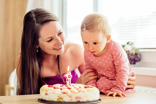 Mother holding her baby daughter with birthday cake