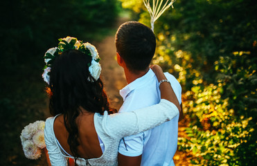 Walk a happy young couple on the nature outside the city. Beautiful and nice young couple stands on a hill in a pine forest in the summer sun