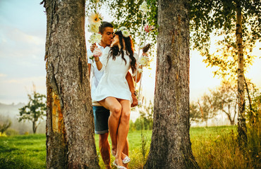 Young kissing couple under big tree with swing at sunset