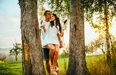 Young kissing couple under big tree with swing at sunset