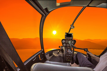 Helicopter cockpit on the sea at sunset, with pilot arm and control board inside the cabin