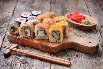 Homemade sushi with salmon, smoked eel, curd cheese and vegetables on a wooden background