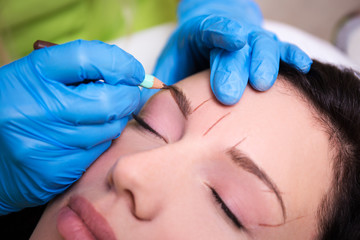 Obraz na płótnie Canvas cosmetician preparing young woman for permanent eyebrow make up