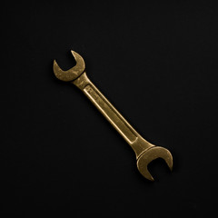 Golden wrench isolated on black background. Symbolic repair tool