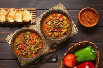 Vegan goulash made of soy meat (textured vegetable protein), capsicum, tomato and onion served in rustic bowls, photographed overhead on dark wood with natural light