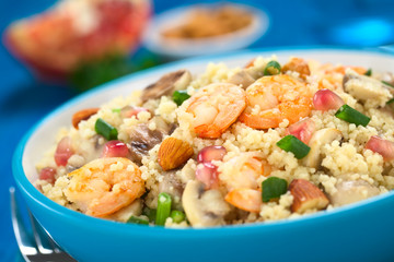 Fototapeta na wymiar Couscous dish with shrimps, mushroom, almond, pomegranate seeds and green onion served in blue bowl (Selective Focus, Focus on the tails of the shrimps on the top of the meal)