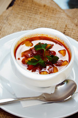 Beautiful red soup with sausage in a white plate with spoon and saucer. Restaurant supply