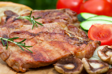Close up of grilled pork ribs served with mushrooms and tomato on wooden plate