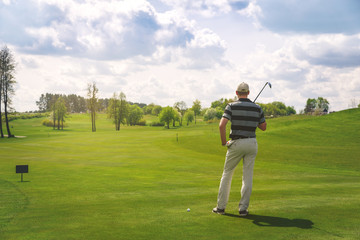 male golfer standing at fairway on golf course, back view