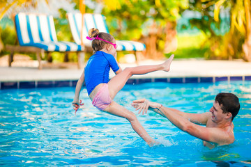 Naklejka premium Little girl and happy father having fun in outdoors swimming pool