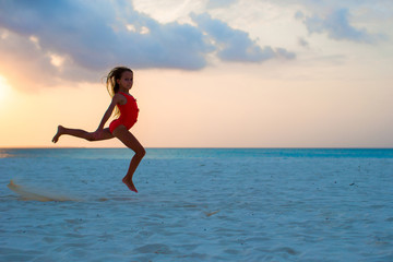 Fototapeta na wymiar Active little girl jumping on white beach at sunset