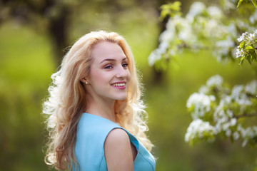 beautiful young blonde woman looks around, smiling.Portrait of a girl in a flowered garden