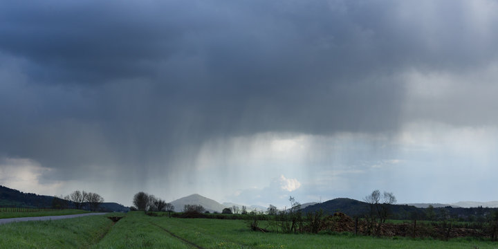 Un paysage de campagne au bord d'une route avec des nuages libérant la pluie au loin