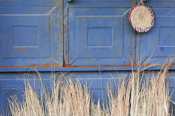 Blue metallic door-wicker underplate-brooms beneath. Mekelle-Ethiopia. 0462