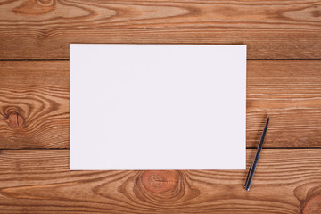 Top view on light wooden office desk with paper and pen.