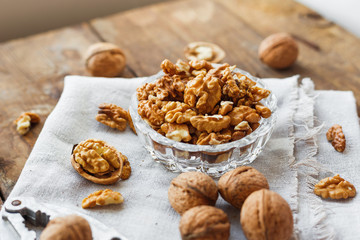 Glass bowl with walnuts on rustic homespun napkin. Healthy snack on old wooden background.