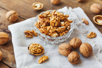 Glass bowl with walnuts on rustic homespun napkin. Healthy snack on old wooden background.