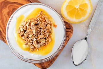 Bowl of lemon flavored yogurt and granola, overhead scene on white marble