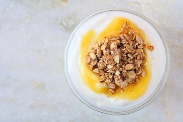 Lemon flavored yogurt with granola, overhead view on white marble background