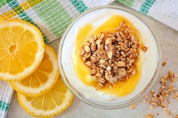 Lemon flavored Greek yogurt with granola, overhead view with towel on white marble