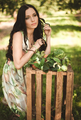 Woman in colorful maxi dress with box with apples in a sunny gar