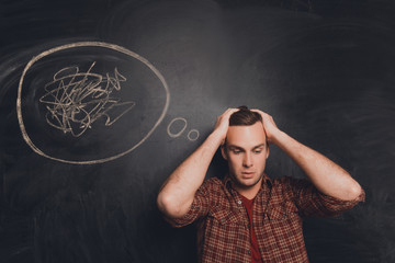 Young tired man at a loss on the background of chalkboard