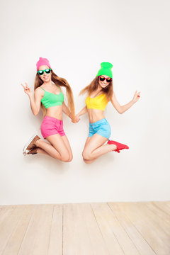 Two happy hipster women in hats and glasses jumping