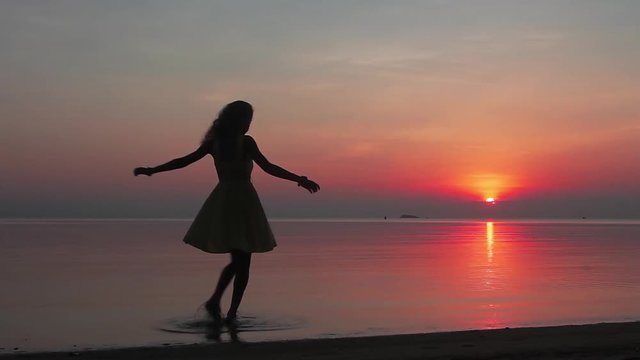 Silhouette of happy young woman whirling at the beach on sunset. Slow motion