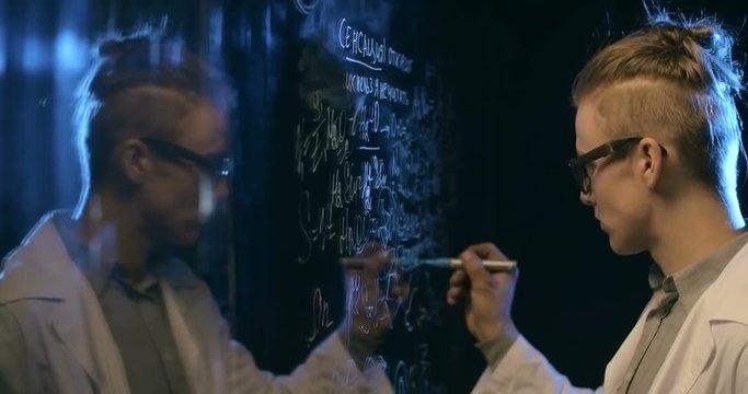 Talented young scientist writing formulas on glass wall and then wiping them off