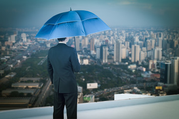 Back view of businessman with umbrella on the rooftop and lookin