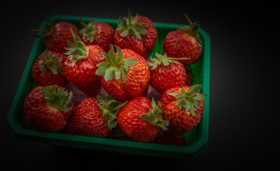 Natural looking strawberries in a green plastic box on dark background. Selective focus.