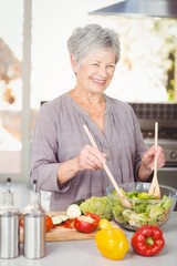 Happy senior woman tossing salad while standing in kitchen