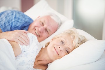 Obraz na płótnie Canvas Portrait of smiling senior woman relaxing besides man on bed