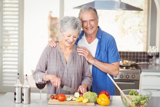 Happy senior man standing with woman cutting salad