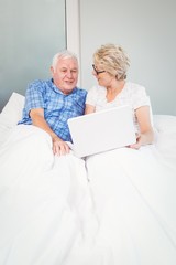 Senior couple with laptop on bed