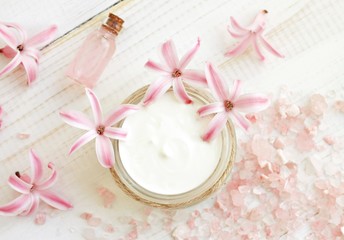 Obraz na płótnie Canvas White body cream in jar, scented sea salt, essential oil, fresh pink flowers. Spa top view.