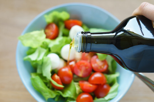 Olive oil being poured onto green salad with tomatoes and mozzarella. Selective focus.