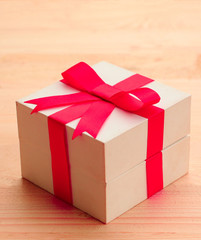 Gift box with red bow on wooden background.